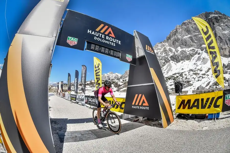 Tom Cooling riding through the Haute Route Dolomites arch with snowy peaks behind