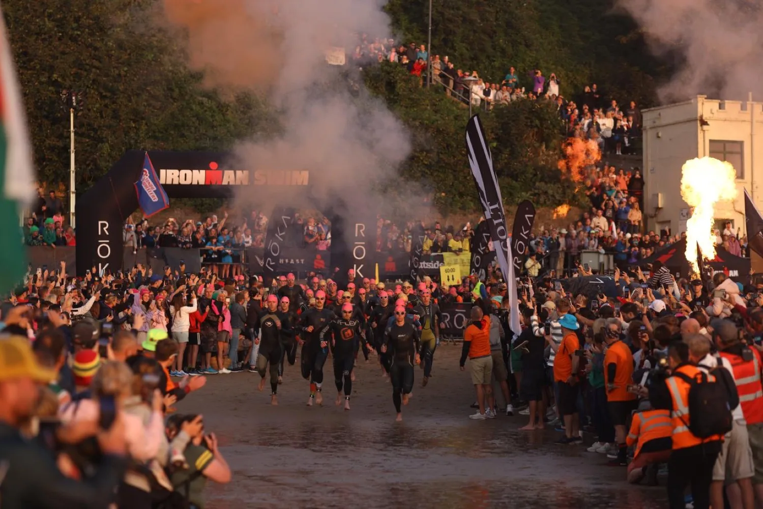 Dawn over Tenby North Beach on Ironman Wales race morning, an orange sky above the sea as athletes gather for the swim start