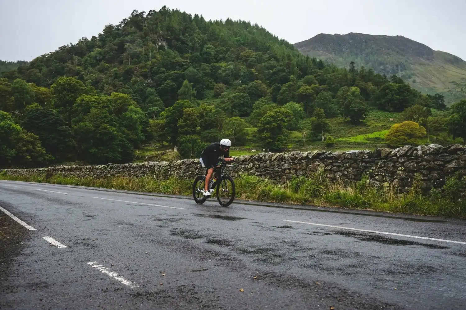 A time triallist riding hard past a stone wall on a wet mountain road