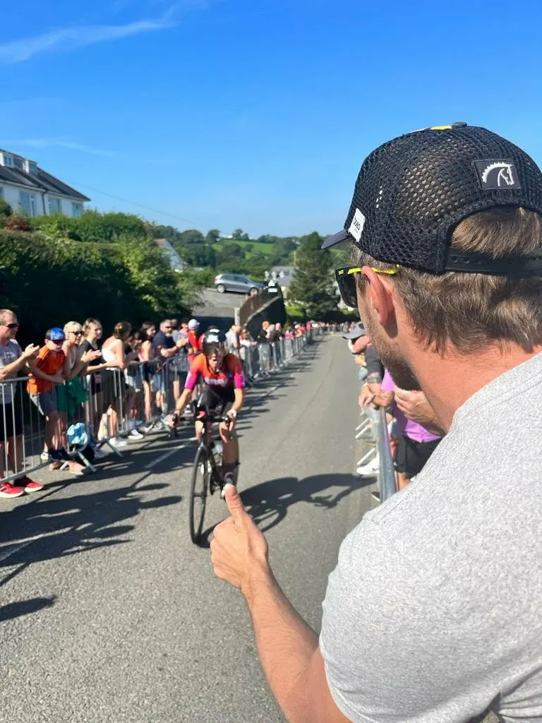 Tom Cooling in a Horsepower cap giving a thumbs up to a racing athlete from the roadside on the Ironman Wales bike course