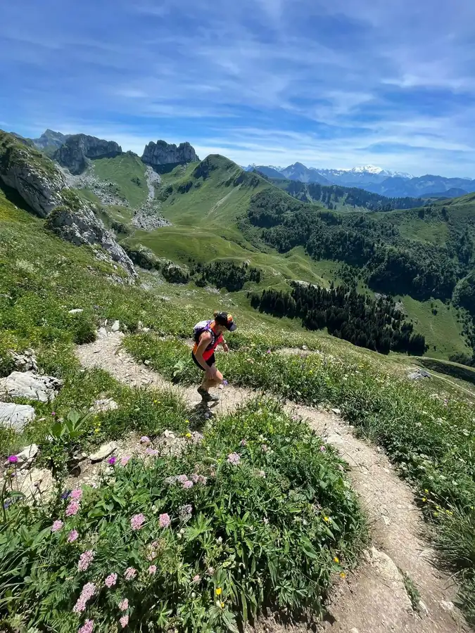 A trail runner on a mountain path with an alpine range behind