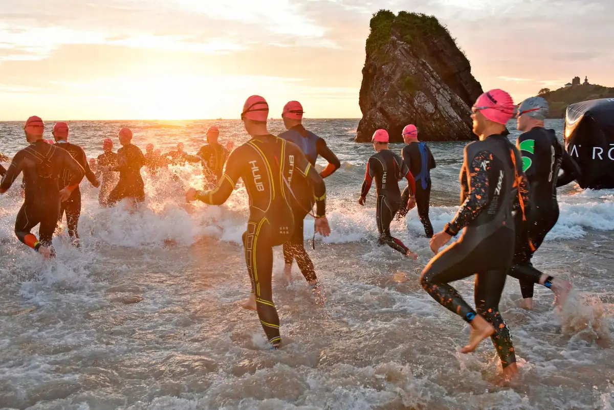 Swimmers in wetsuits and pink caps charging into the sea at the Ironman Wales swim start at sunrise