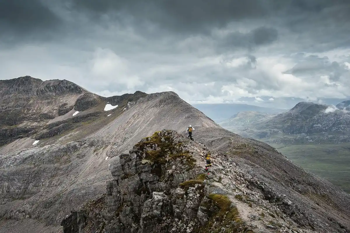 Two runners crossing a rocky Torridon ridge under a brooding sky