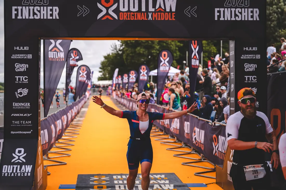 Elly B finishing the Outlaw triathlon, arms out on the finish carpet