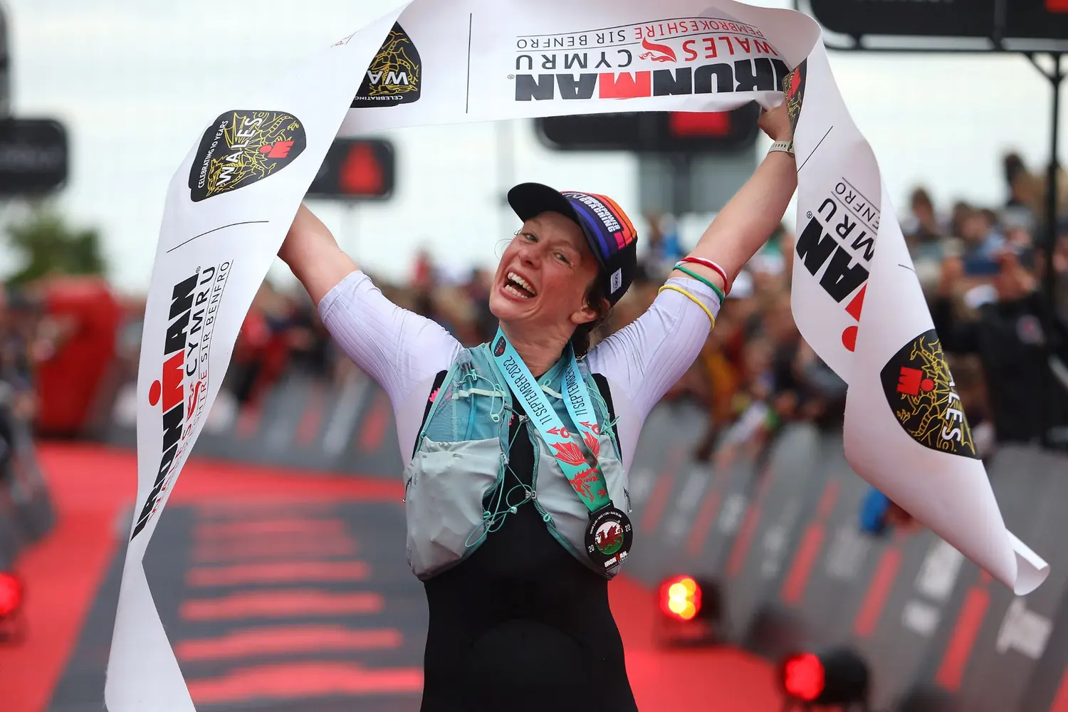 An athlete crossing an Ironman finish line in Wales with arms wide